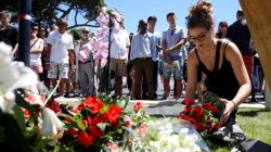A woman places a bouquet of flowers as people pay tribute near the scene where a truck ran into a crowd at high speed killing scores and injuring more who were celebrating the Bastille Day national holiday in Nice