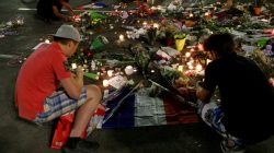 People react near flowers placed on the road in tribute to victims, three days after an attack by the driver of a heavy truck who ran into a crowd on Bastille Day killing scores and injuring as many on the Promenade des
