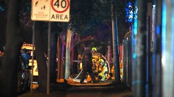 A bomb disposal expert wearing protective gear walks past emergency services personnel outside a police station in the western Sydney suburb of Merrylands, Australia