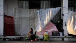 A woman sits and looks on outside a building covered up with sheets to protect the dwellers from the strong summer sun outside of the disused Hellenikon airport, where stranded refugees and migrants are temporarily accommodated in Athens, Greece,