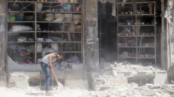 A civilian removes the rubble in front of a damaged shop after an airstrike in the rebel held al-Saleheen neighborhood of Aleppo,