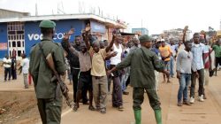 Congolese soldiers stand guard as civilians chant slogans during a protest against the government's failure to stop the killings and inter-ethnic tensions in the town of Butembo