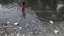 A boy searches for coins thrown by devotees as religious offerings in a polluted water channel near a temple in Kolkata
