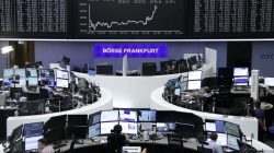 Traders work at their desks in front of the German share price index, DAX board, at the stock exchange in Frankfurt, Germany,