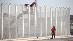 Workers set-up barbed wires on top of a fence along the harbour of Calais to prevent migrants jumping aboard lorries
