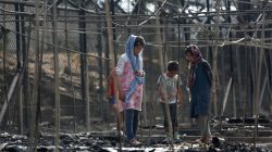 Migrants stand among the remains of a burned tent at the Moria migrant camp, after a fire that ripped through tents and destroyed containers during violence among residents, on the island of Lesbos, Greece,