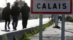 Migrants pass by a road sign as they leave the northern area of the camp called the "Jungle" in Calais, France,