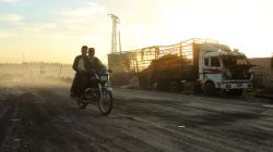 Men drive a motorcycle near a damaged aid truck after an airstrike on the rebel held Urm al-Kubra town, western Aleppo city, Syria September 20, 2016.