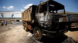 People walk near a torched truck in the compound of a textile factory damaged by protests in the town of Sebeta, Oromia region, Ethiopia,