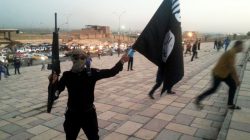 A fighter of the Islamic State of Iraq and the Levant (ISIL) holds an ISIL flag and a weapon on a street in the city of Mosul