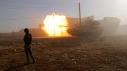 A rebel fighter stands near a Turkish tank as it fires towards Guzhe village, northern Aleppo countryside, Syria