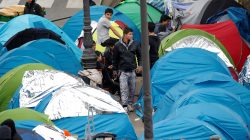 Migrants stand near their tents at a makeshift migrant camp on a street near the metro stations of Jaures and Stalingrad in Paris.