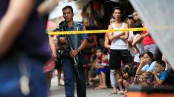 A member of the Philippine National Police (PNP) stands guard while residents look on near the scene where two suspected drug pushers were killed during a police operation, in metro Manila, Philippines