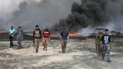 Tribal fighters walk as fire and smoke rises from oil wells, set ablaze by Islamic State militants before IS militants fled the oil-producing region of Qayyara, Iraq,