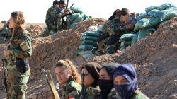 Iranian-Kurdish female fighters sit near a sand berm during a battle with Islamic State militants in Bashiqa, near Mosul, Iraq