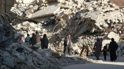 People walk past rubble of damaged buildings in a rebel-held besieged area in Aleppo, Syria
