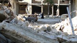 People walk past rubble of damaged buildings in a rebel-held besieged area in Aleppo, Syria