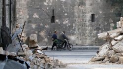 A man walks past a man riding a bicycle near the rubble of damaged buildings in the rebel held area of Old Aleppo, Syria