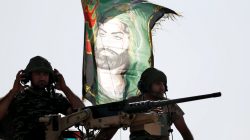 Iraqi special forces soldiers sit on top of an armoured vehicle next to a flag of Imam Hussein in Bartella, east of Mosul, Iraq