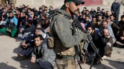 Men sit on the ground as an Iraqi Special forces intelligence team check their ID cards as they search for Islamic State fighters in Mosul, Iraq