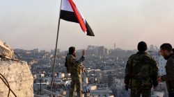 A Syrian government soldier gestures a v-sign under the Syrian national flag near a general view of eastern Aleppo after they took control of al-Sakhour neigbourhood in Aleppo, Syria