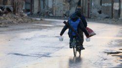 A rebel fighter carries food while riding a bicycle and carrying his weapon on his back in rebel-held besieged old Aleppo,