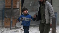 A man holds the hand of a boy as they flee deeper into the remaining rebel-held areas of Aleppo,