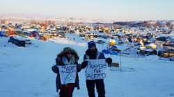 A couple of the remaining activists, hold up signs as they grapple with plunging temperatures that make conditions more difficult at the protest camp in Cannon Ball, North Dakota,
