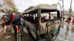 People look at a burned vehicle at the site of car bomb attack in a busy square at Baghdad's sprawling Sadr City district, in Iraq