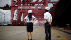 employees stand next to container ship, holding U.S. trade goods