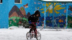 refugee boy rides bike through snow