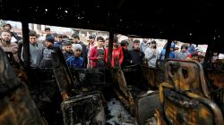 People look into the remains of a car after being bombed