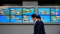 Men walk past an electronic board showing Japan's Nikkei average outside a brokerage in Tokyo, Japan,