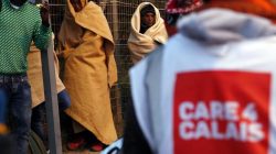An aid worker provides assistance near a group of migrants claiming to be minors who use blankets to protect themselves from the cold as they prepare to spend the night after the dismantlement of the "Jungle" camp in Calais, France, October 27, 2016. REUTERS/Pascal Rossignol