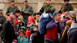 Syrian army soldiers (back L) and Russian soldiers (back R) monitor as rebel fighters and their families evacuate the besieged Waer district in the central Syrian city of Homs, after an agreement was reached between rebels and Syria's army, March 18, 2017. REUTERS/Omar Sanadiki