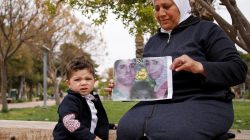 Hajar Saleh poses with her grandson Jaafar as she holds a picture depicting Jaafar's parents, Amina Saleh and her husband Imad Azouz who were killed fleeing Syria's civil war, at a garden in the Damascus district of Mezzeh,