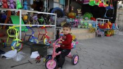 A boy sits on his bicycle in front of a toy store, in eastern Mosul, Iraq