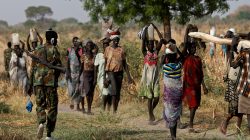 FILE PHOTO: A soldier walks past women carrying their belongings near Bentiu, northern South Sudan, February 11, 2017. REUTERS/Siegfried Modola /File Photo