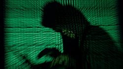 A hooded man holds a laptop computer as cyber code is projected on him in this illustration picture