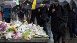 Pedestrians carry umbrellas as they walk past floral tributes to the victims of the recent attack at London Bridge and Borough Market, in central London, Britain June 6, 2017. REUTERS/Toby Melville