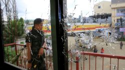 A policeman stands on guard behind a window full of bullet holes as government soldiers assault the Maute group in Marawi City, Philippines