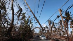 Cars drive under a partially collapsed utility pole, after the island was hit by Hurricane Maria in September, in Naguabo, Puerto Rico