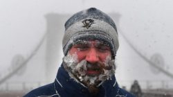 A pedestrian walks through blinding snow across the Brooklyn Bridge in New York City.