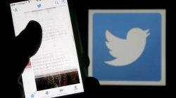 A man reads tweets on his phone in front of a displayed Twitter logo in Bordeaux, southwestern France, March 10, 2016. REUTERS/Regis
