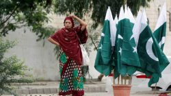 A woman adjusts her scarf as she waits for a bus next to a stall with national flags, ahead of Pakistan's Independence Day, in Karachi, Pakistan August 2, 2017. REUTERS/Akhtar Soomro