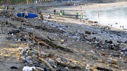 FILE PHOTO: Tourists walk amongst trash washed up on Kuta beach by seasonal winds, as workers attempt a clean-up in the background, on the Indonesian island of Bali February 15, 2016 in this photo taken by Antara Foto. REUTERS/Wira Suryantala/Antara Foto