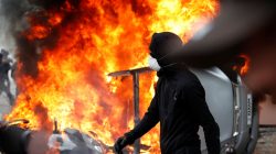 A masked protester walks near a car that burns outside a Renault automobile garage during clashes during the May Day labour union march in Paris, France, May 1, 2018. REUTERS/Christian Hartmann