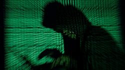 A hooded man holds a laptop computer as cyber code is projected on him in this illustration picture taken on May 13, 2017. REUTERS/Kacper Pempel/Illustration