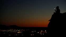 FILE PHOTO: A young couple look at their phone as they sit on a hillside after sun set in El Paso, Texas, U.S., June 20, 2018. REUTERS/Mike Blake