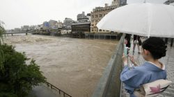 A kimono-clad woman using a smartphone takes photos of swollen Kamo River, caused by a heavy rain, from Shijo Bridge in Kyoto, western Japan, in this photo taken by Kyodo July 5, 2018. Mandatory credit Kyodo/via REUTERS